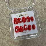 Set of red nail art designs with white flowers in a clear case on a textured surface.
