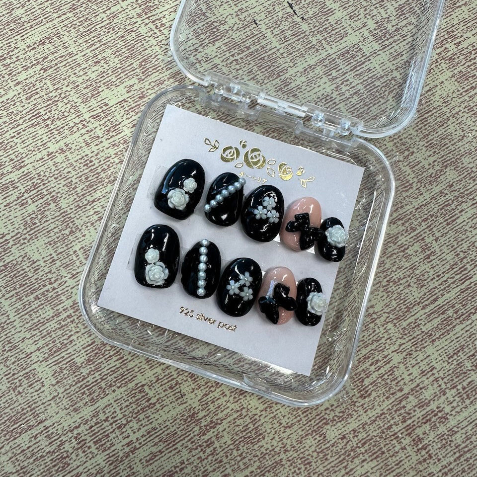 Set of black and white nail art samples in a clear display case on a textured surface.